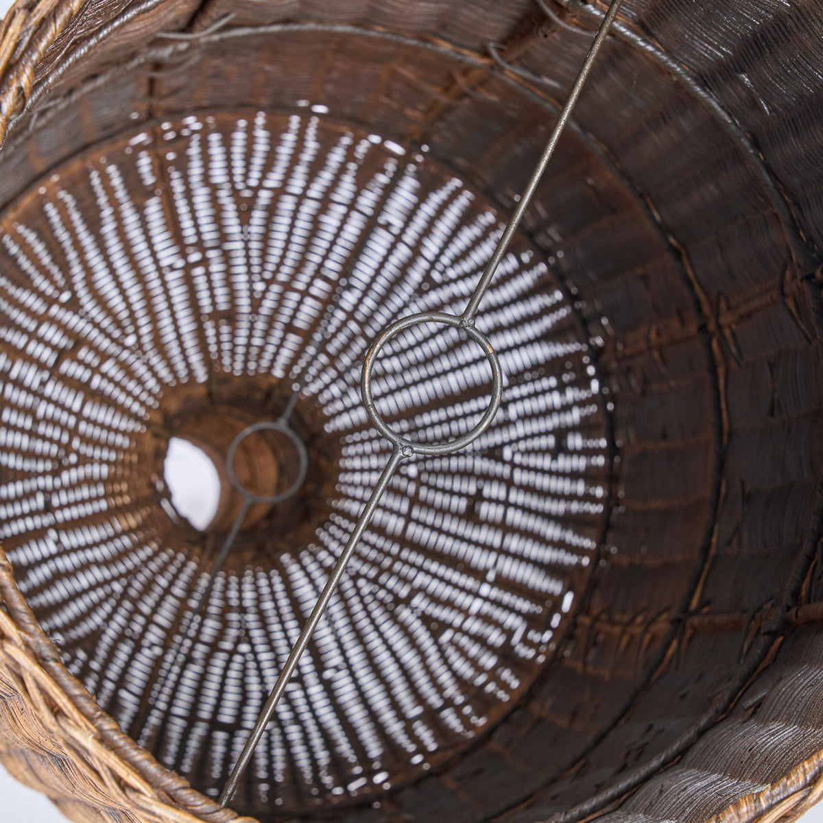 Close up of a woven wicker light shade with a metal handle on a white background