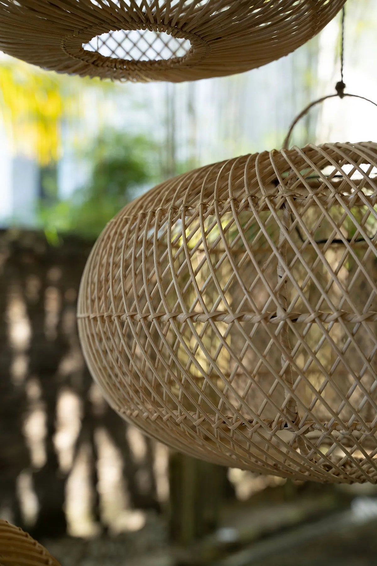 Woven rattan lampshades hanging against a blurred natural background