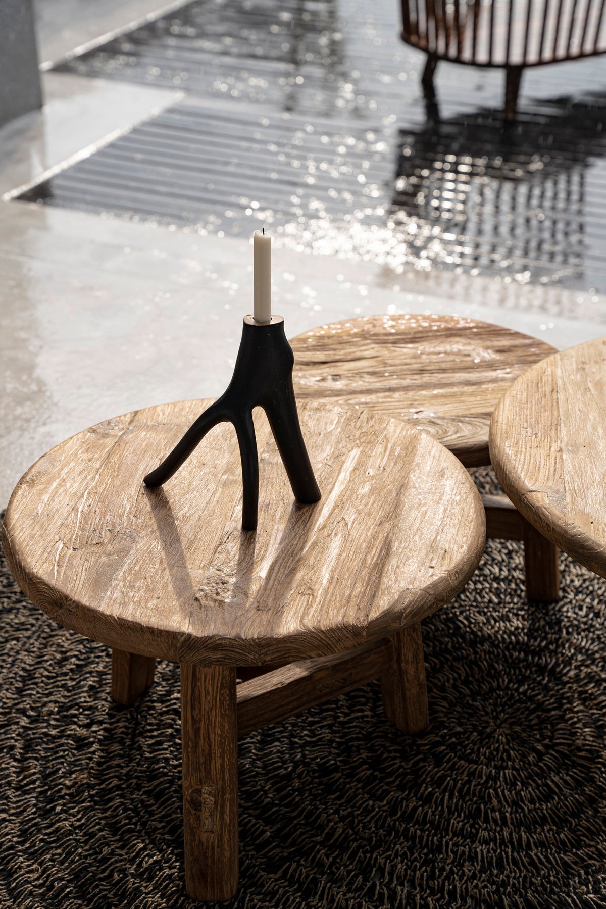 Wooden coffee table with a candle holder and candle on a textured floor.