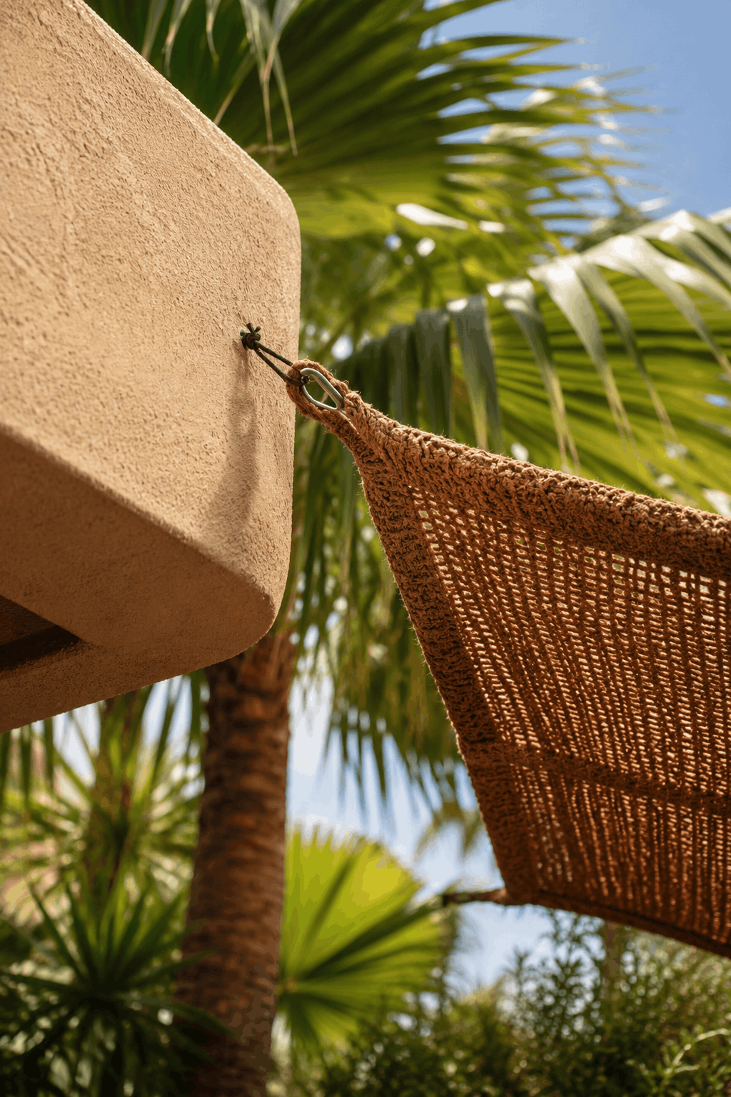 Hanging sunshade sail attached to a wall with palm trees in the background