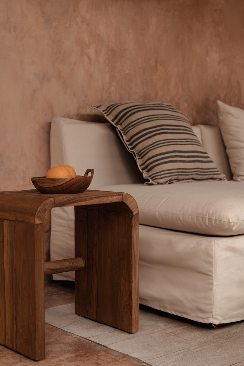 Teak wood side table in natural living room with plaster walls and linen sofa