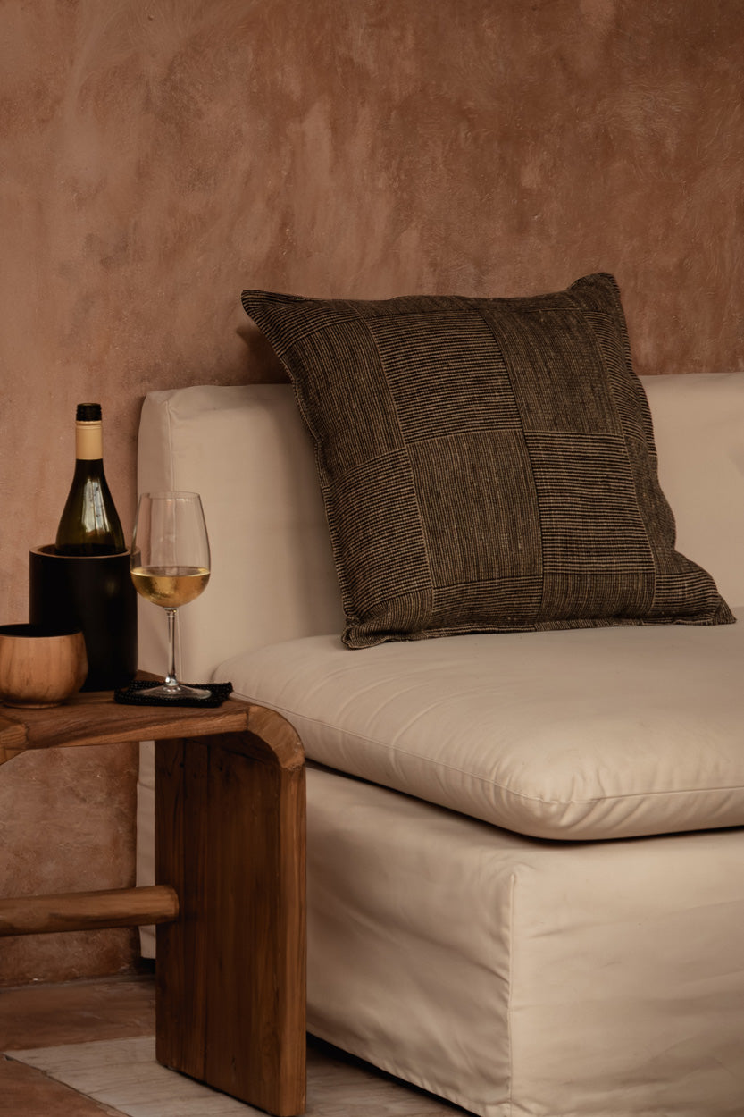 Teak wood side table in natural living room with plaster walls and linen sofa and dark cushions