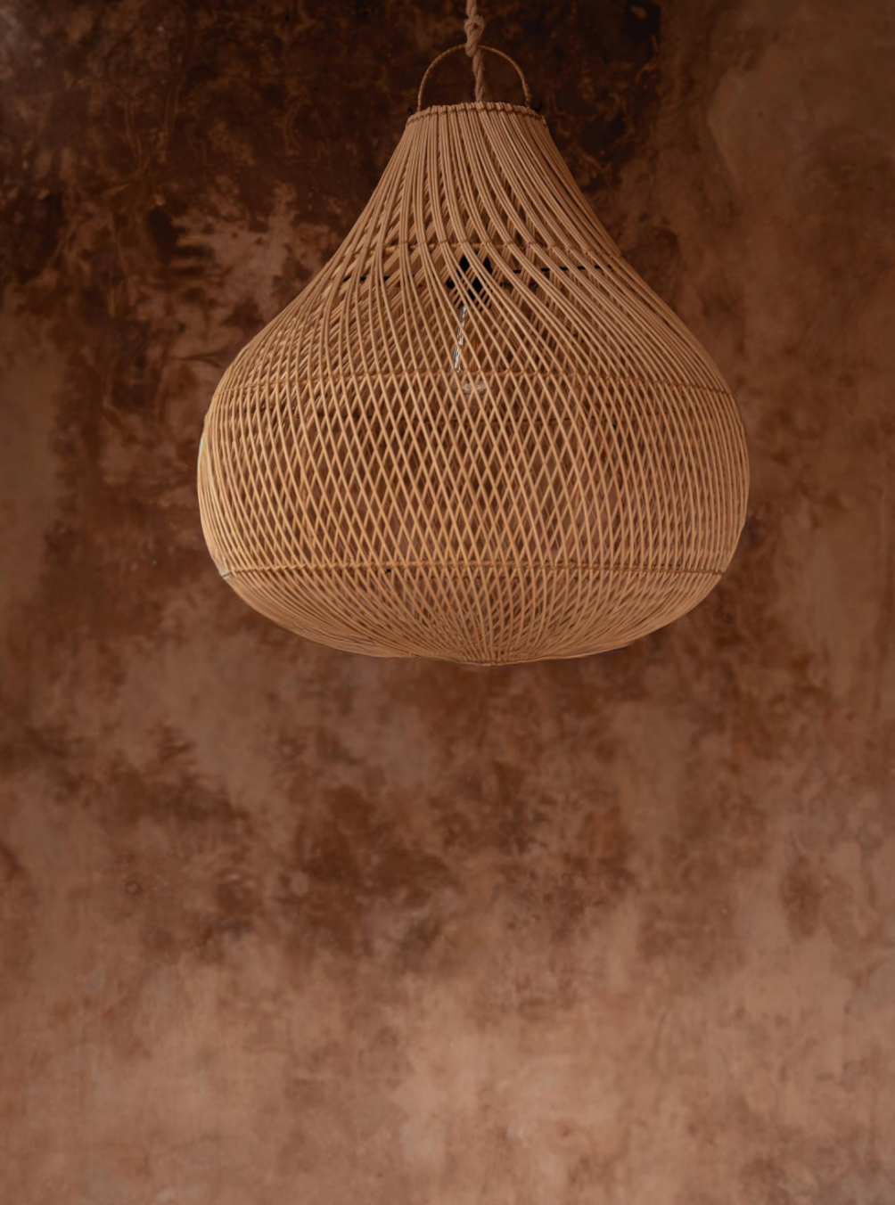 Natural woven rattan pendant light against a textured brown wall