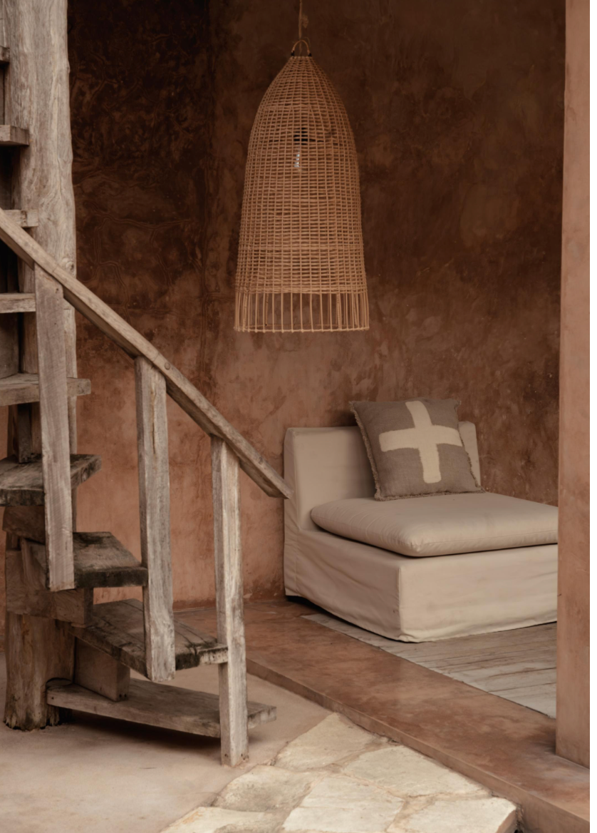 Wabi sabi interior with a textured wall, wooden staircase, and a cushioned chair.