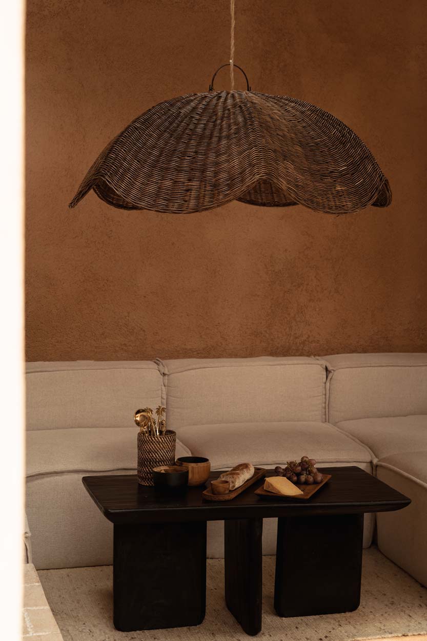 Extra large rattan wicker pendant light shade hanging above a coffee table with decor items in a room with a beige sofa and wall.