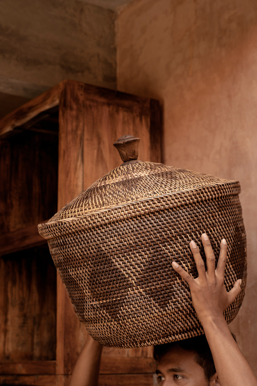 Person holding a woven laundry basket above their head in a rustic setting