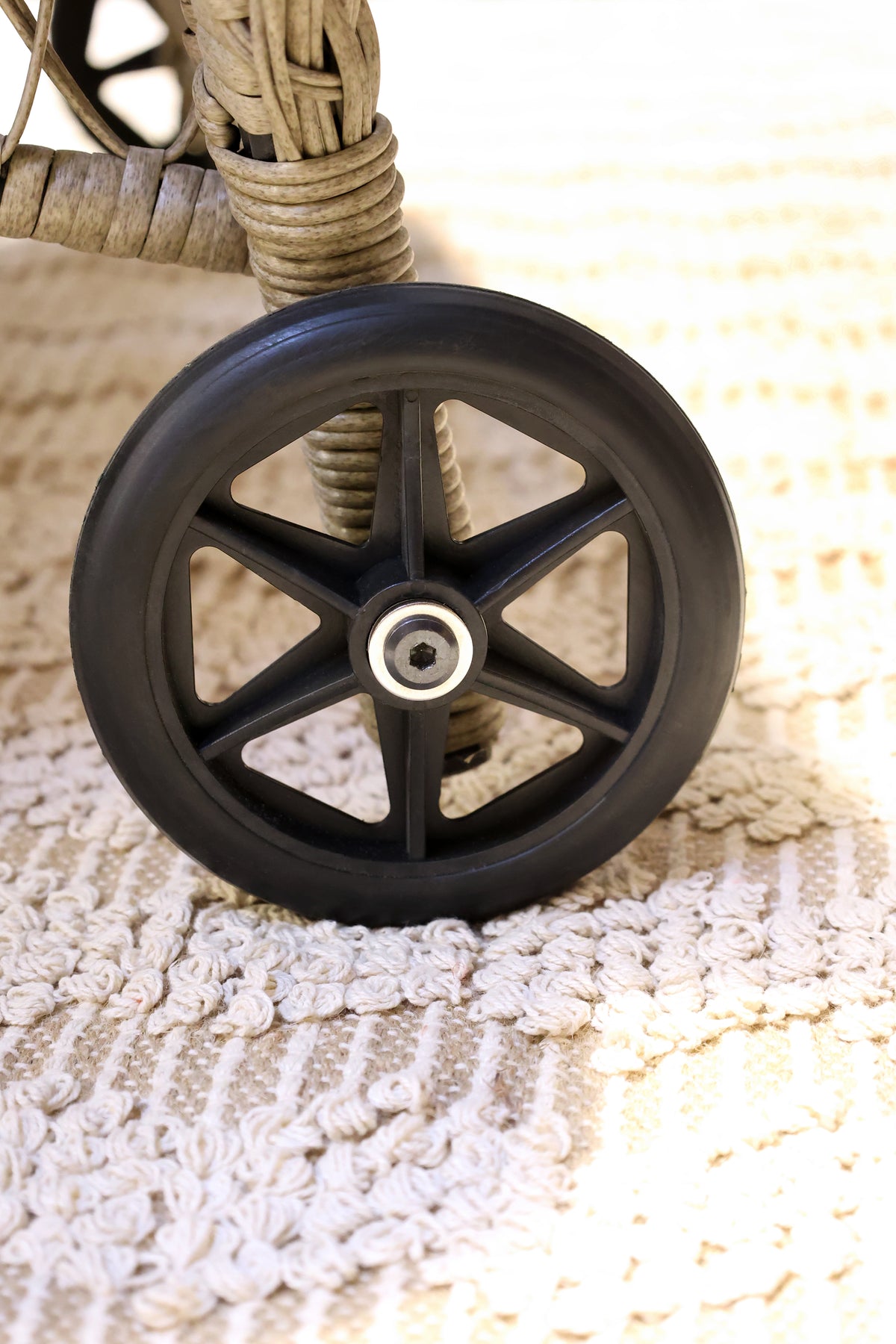 Close up of a black wheel with metal hub of a wicker rattan sun lounger
