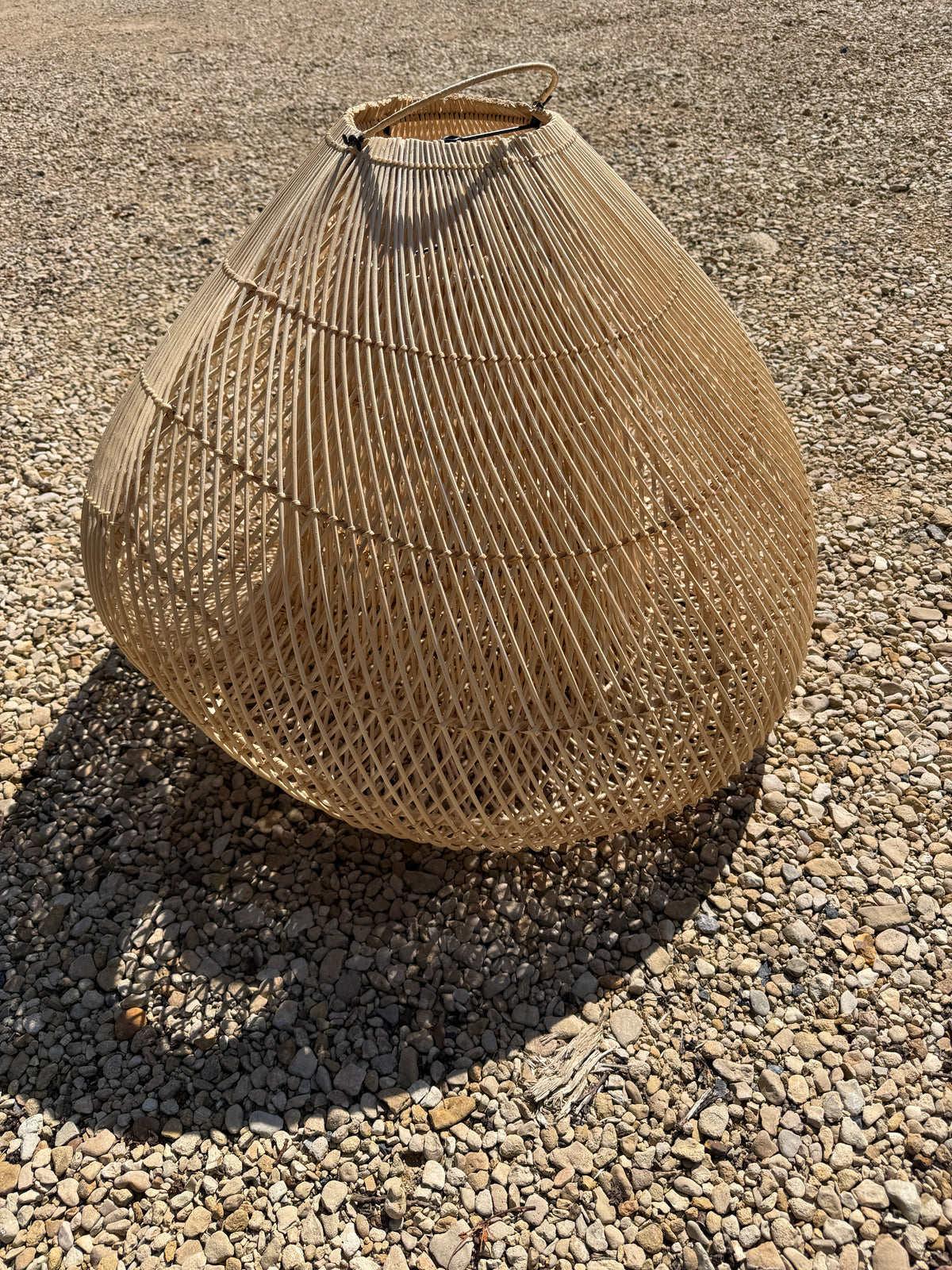 Textured brown rattan wicker basket shade on a gravel surface