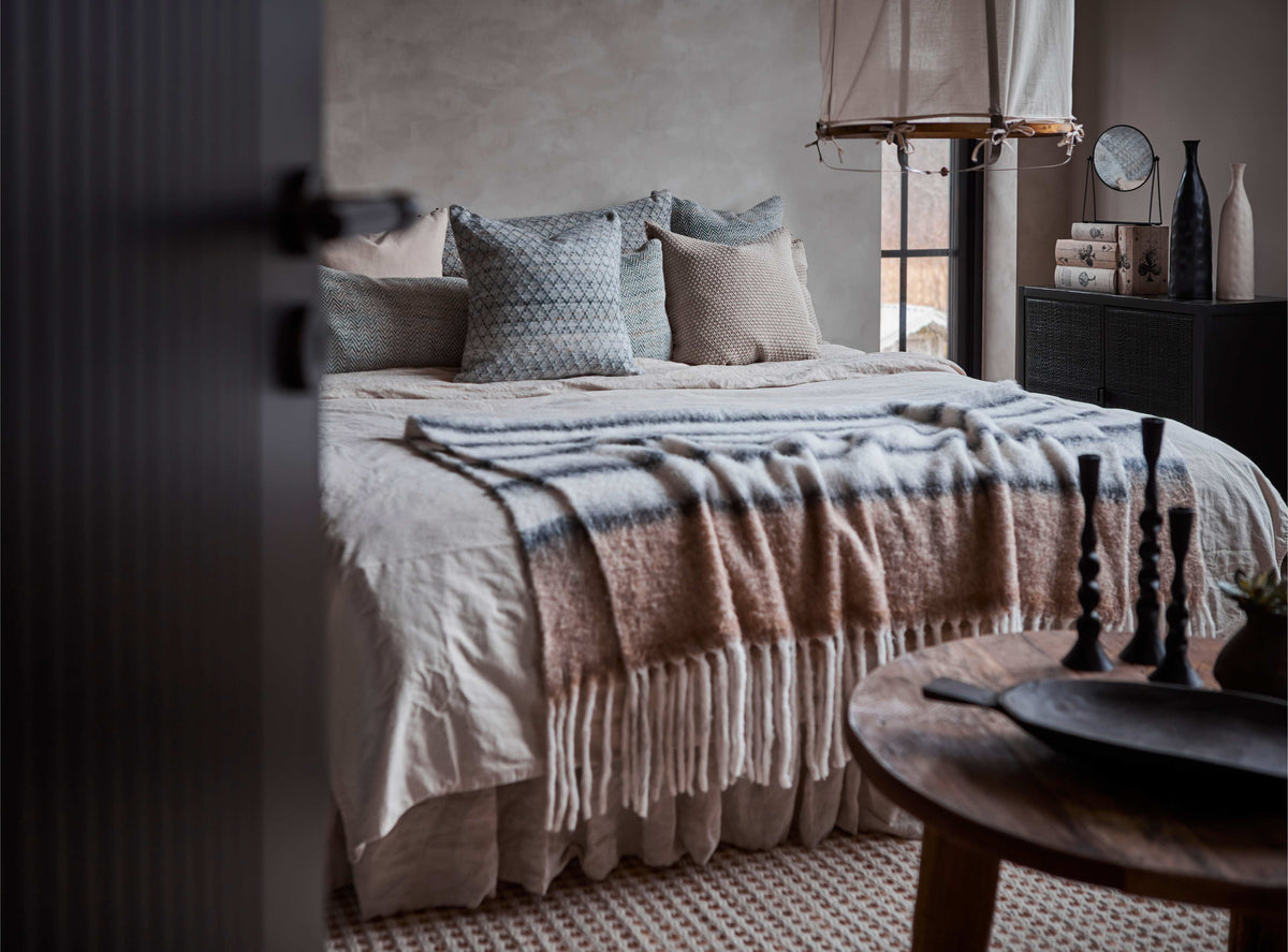 Cosy bedroom with a bed covered in a blanket and pillows, a side table with candles, and decor items.
