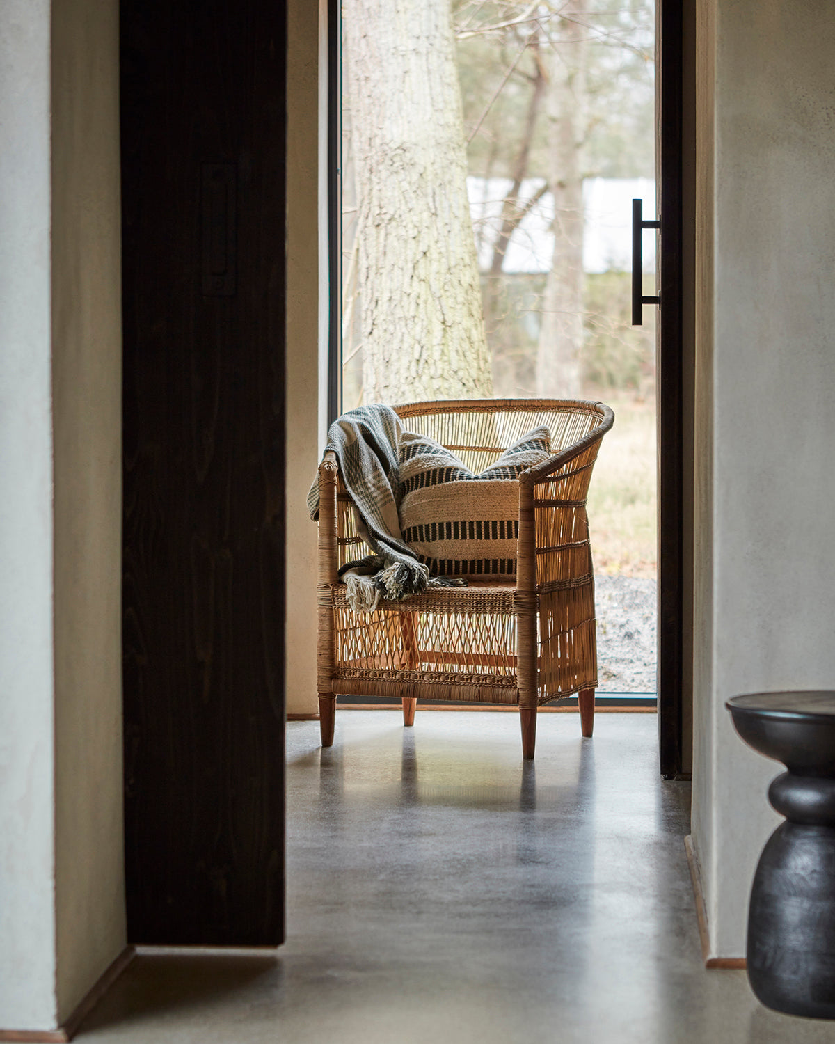Wicker chair with a blanket and 50cm cushion n a room with a large window.