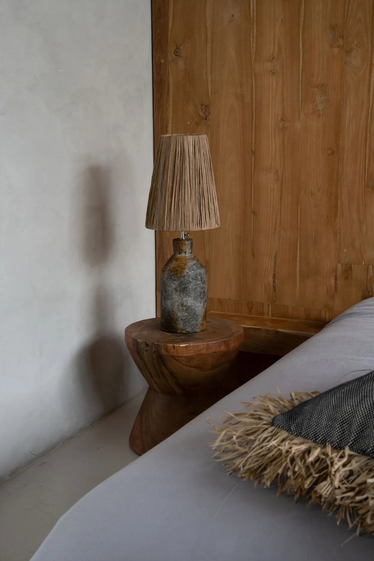 Nestled corner of a bedroom with a wooden side table and lamp against a wooden wall.