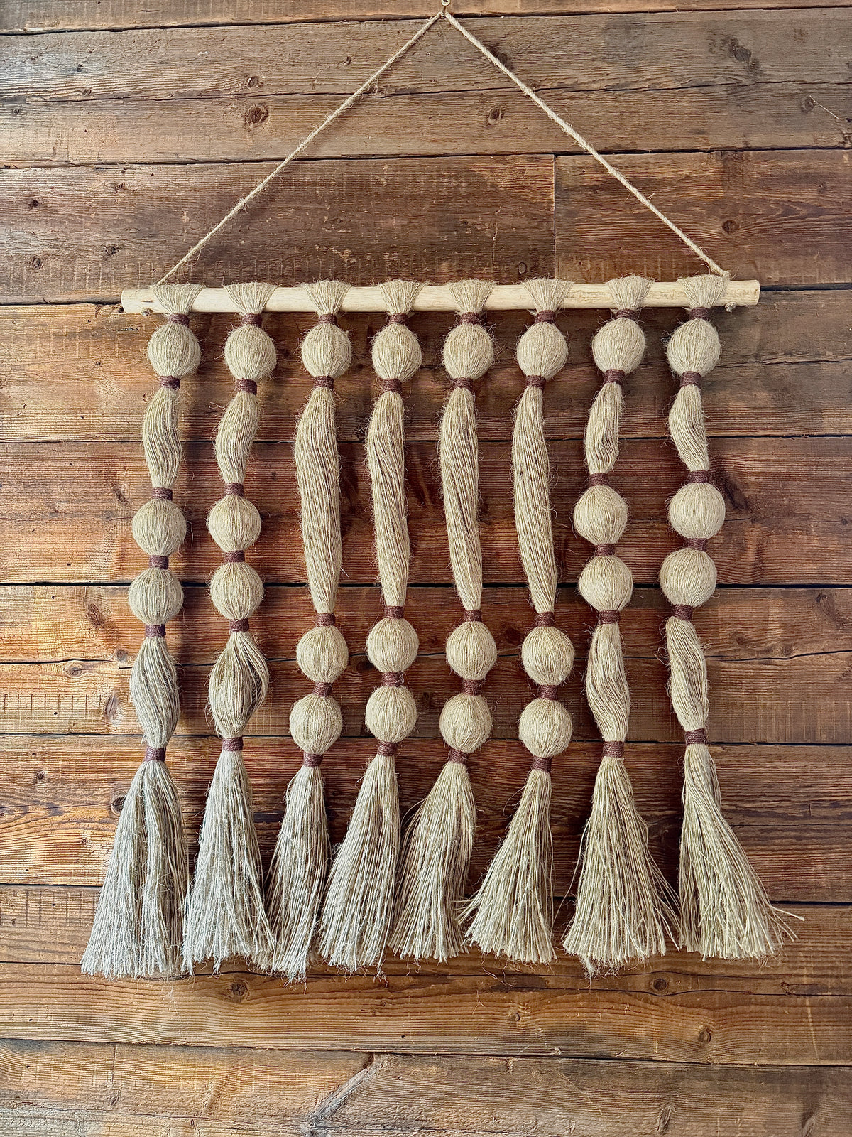Textile wall hanging with tassels on a wooden wall