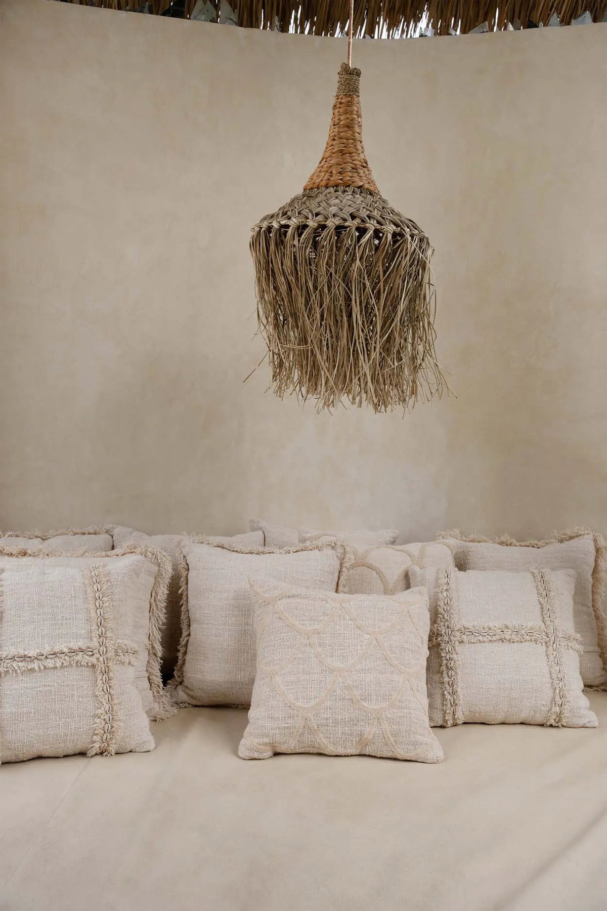 Textured cushions on a sofa with a woven rattan natural pendant light against a beige wall.