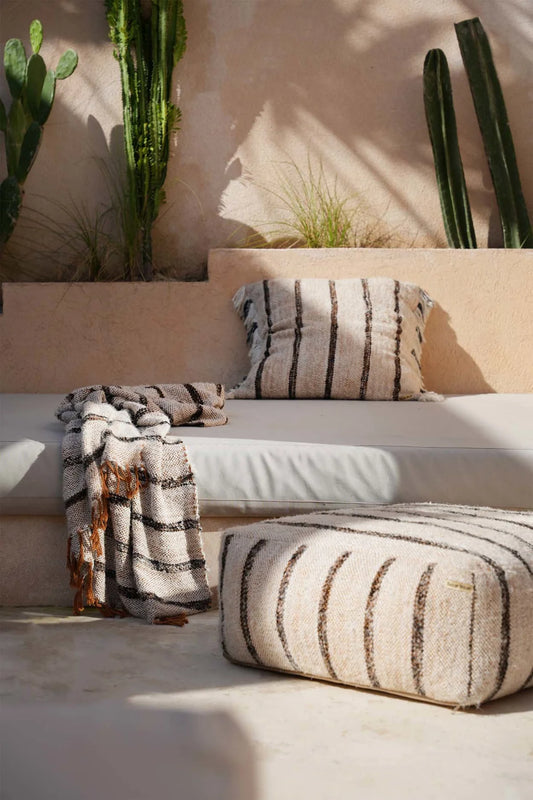 Outdoor seating area with striped cushions and a blanket, surrounded by cacti.