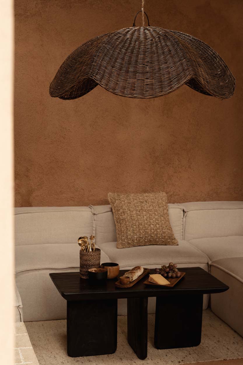 Living room with a wicker pendant light, beige sofa, and coffee table with snacks.