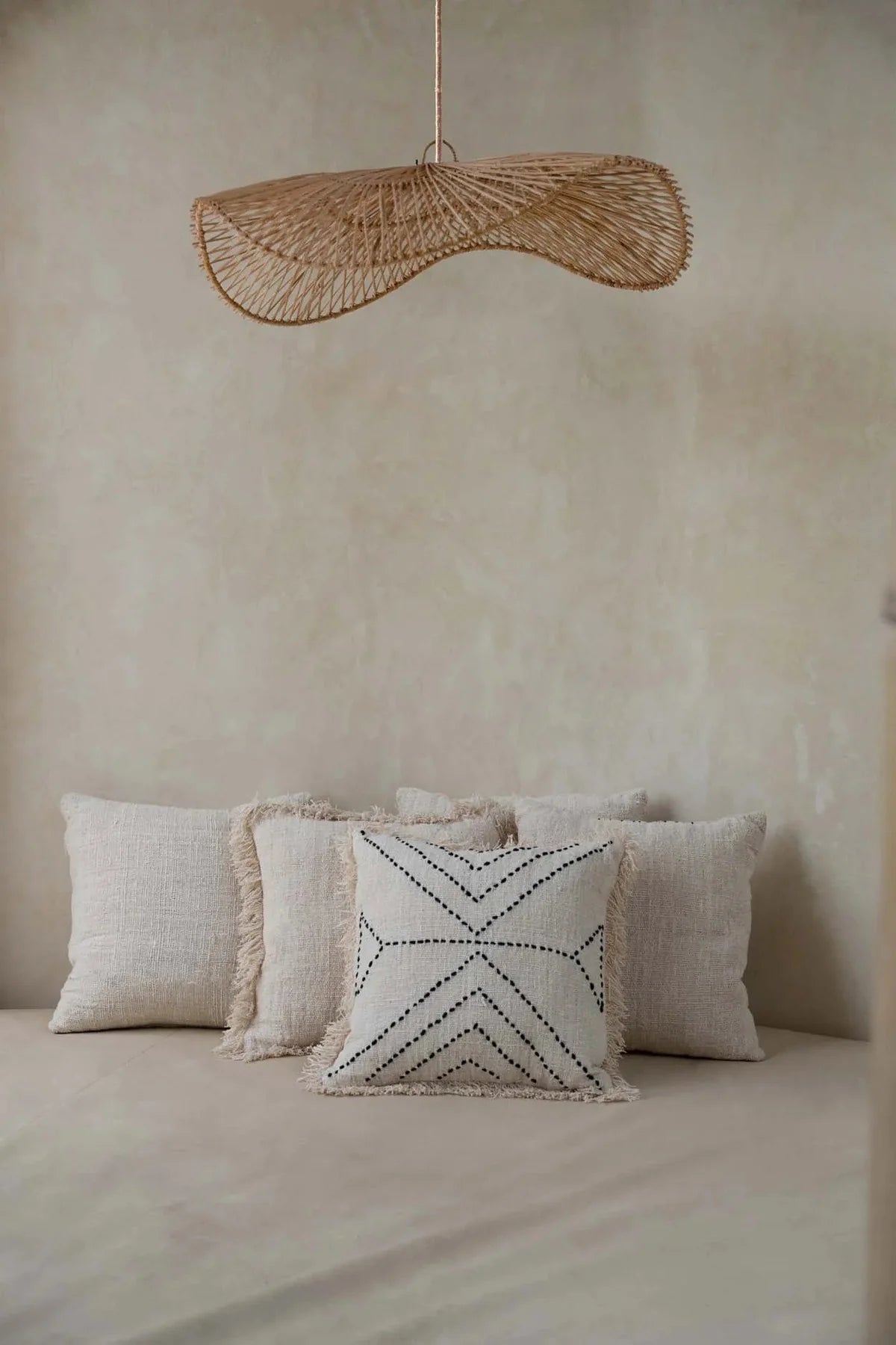 Decorative pillows on a bed with a large woven rattan flat pendant light fixture above.