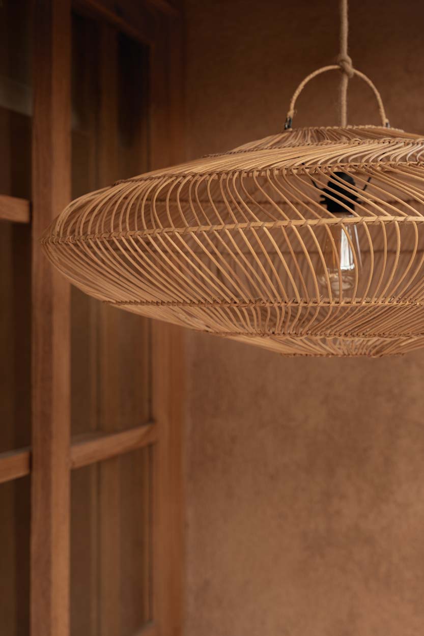 Woven rattan pendant light hanging against a warm toned living room wall.