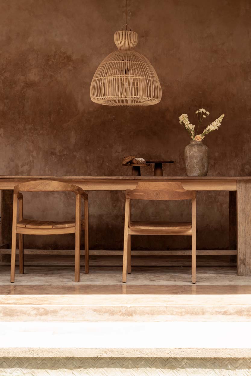 Large rattan pendant light above a wooden dining table with chairs against a textured brown wall.