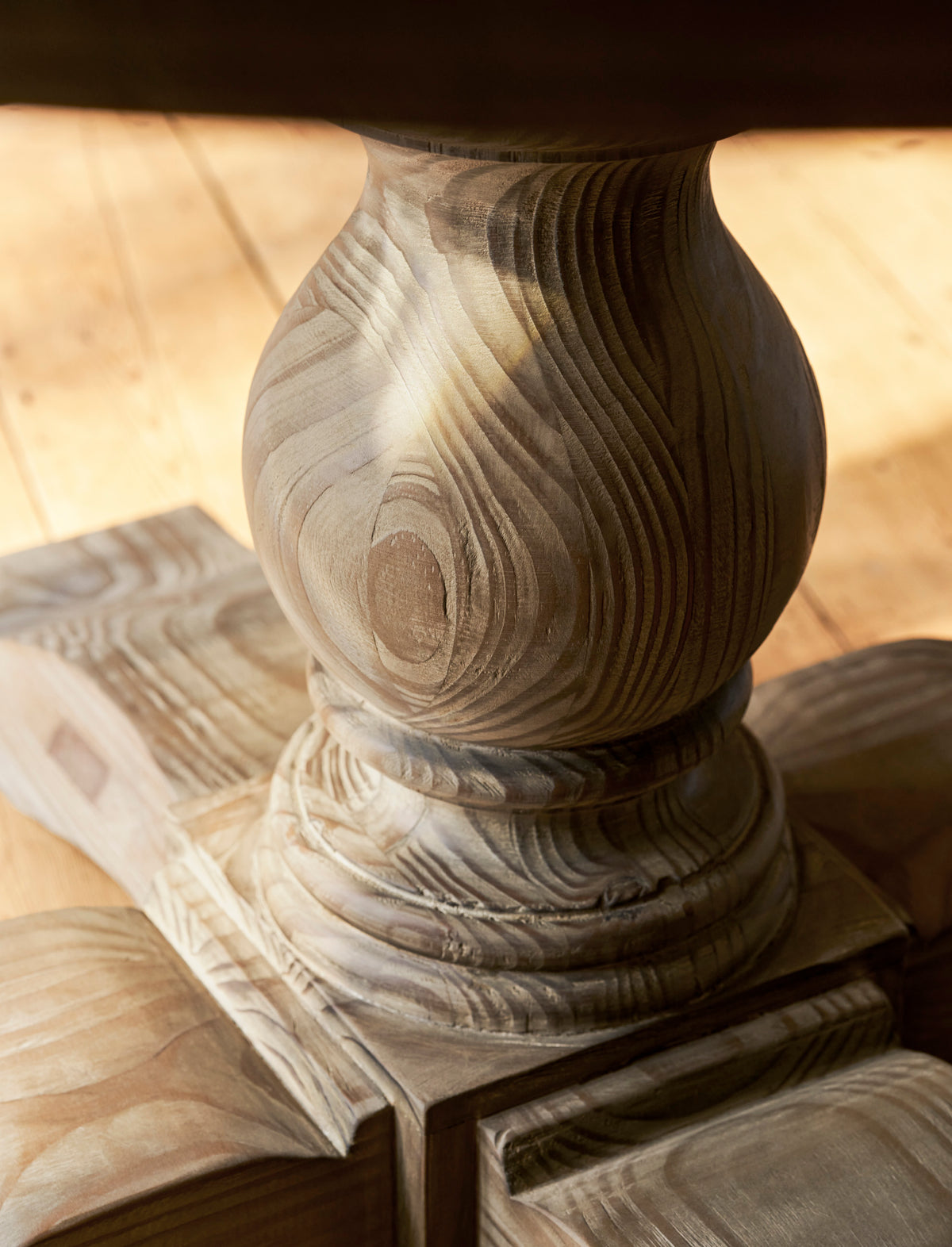 Close up of a wooden pedestal with intricate carvings on a wooden surface.