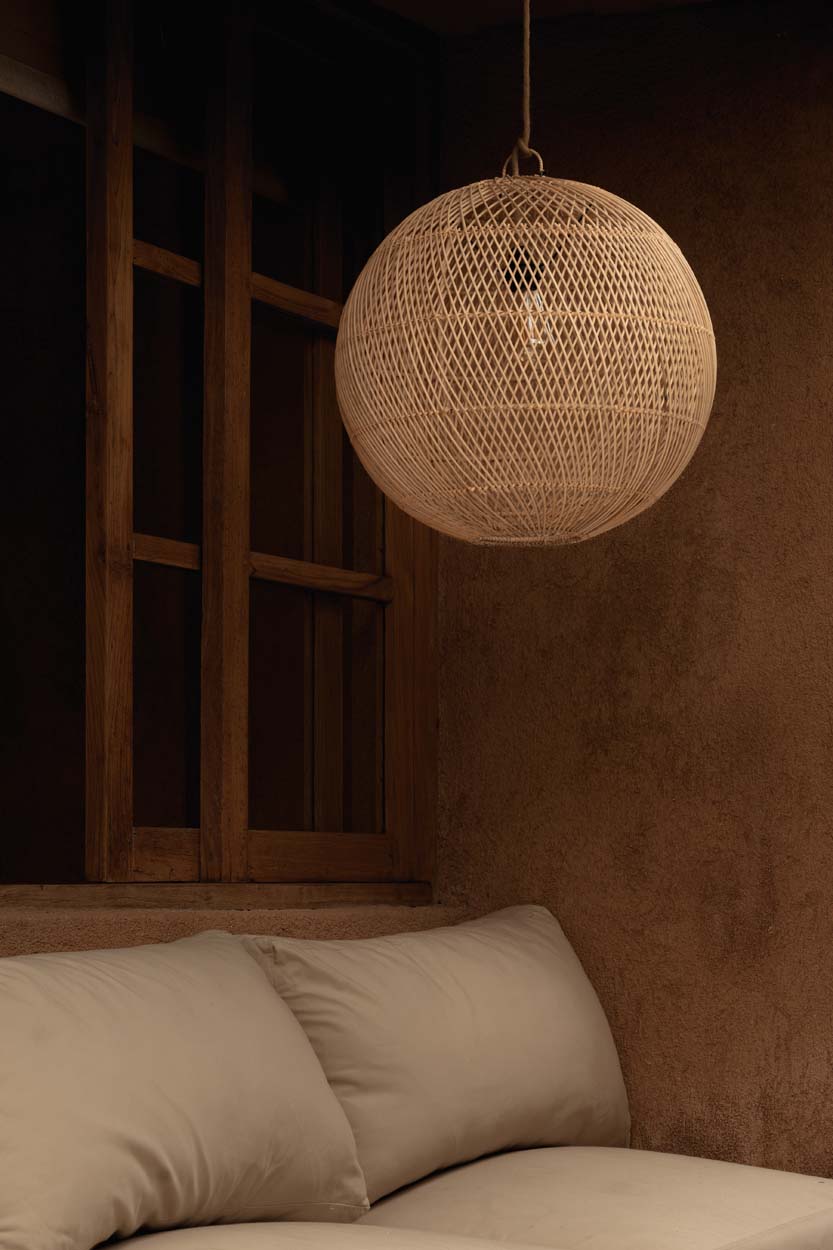 Woven rattan round pendant light hanging above a sofa with a wooden shelf in the background.