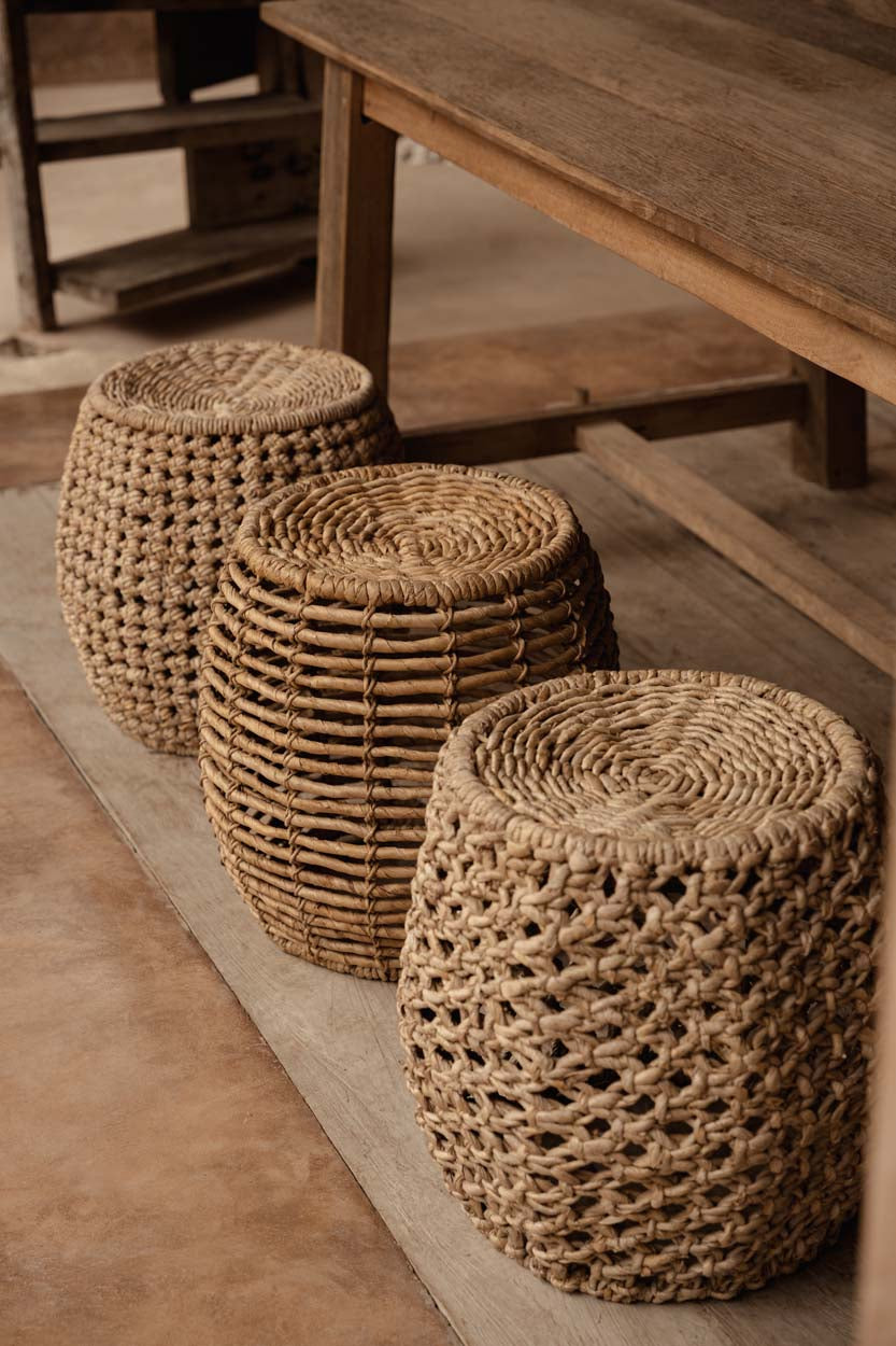 Three natural woven stools on a wooden floor with a wooden table in a rustic kitchen dining room