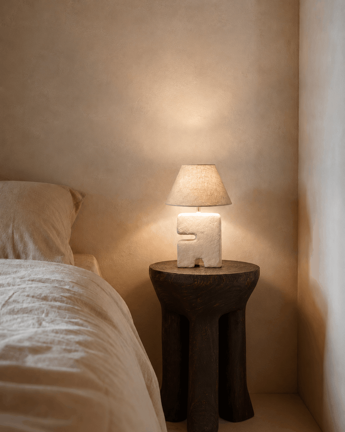 Bedside , space saving small lamp on a wooden side table next to a bed in a softly lit room