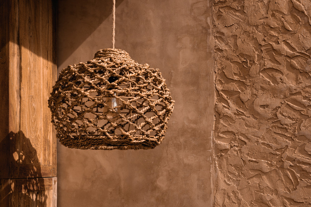 Woven pendant light hanging against a textured terracotta plastered wall.