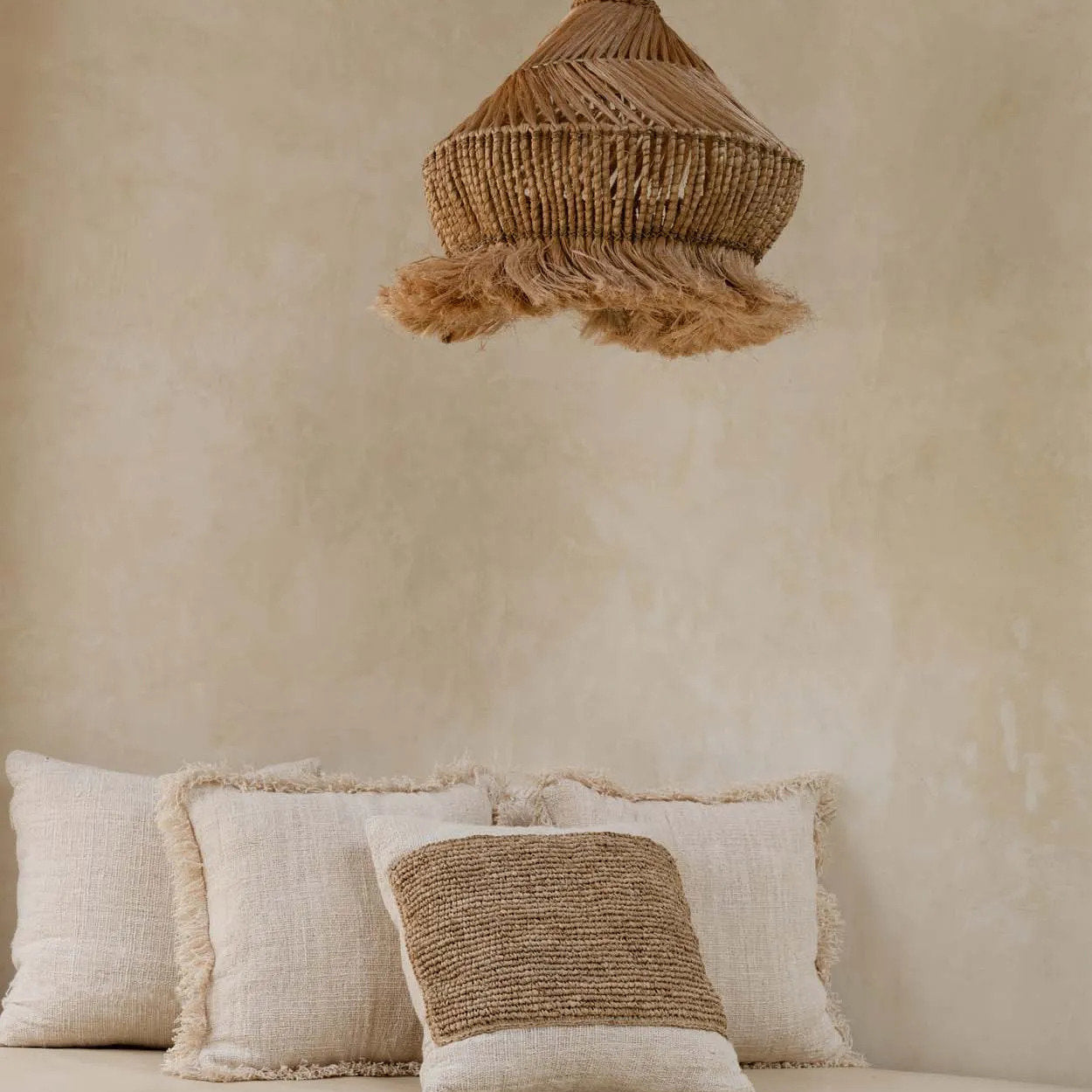 Beige wall with a woven natural pendant light and textured cushions on a bed.