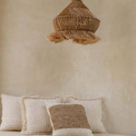 Beige wall with a woven natural pendant light and textured cushions on a bed.