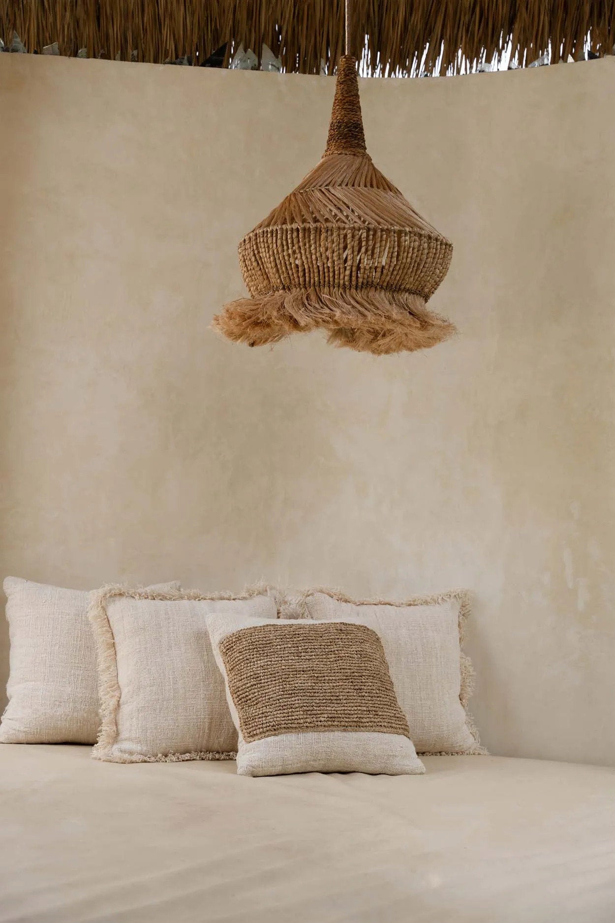 Beige wall with a woven natural pendant light and textured cushions on a bed.