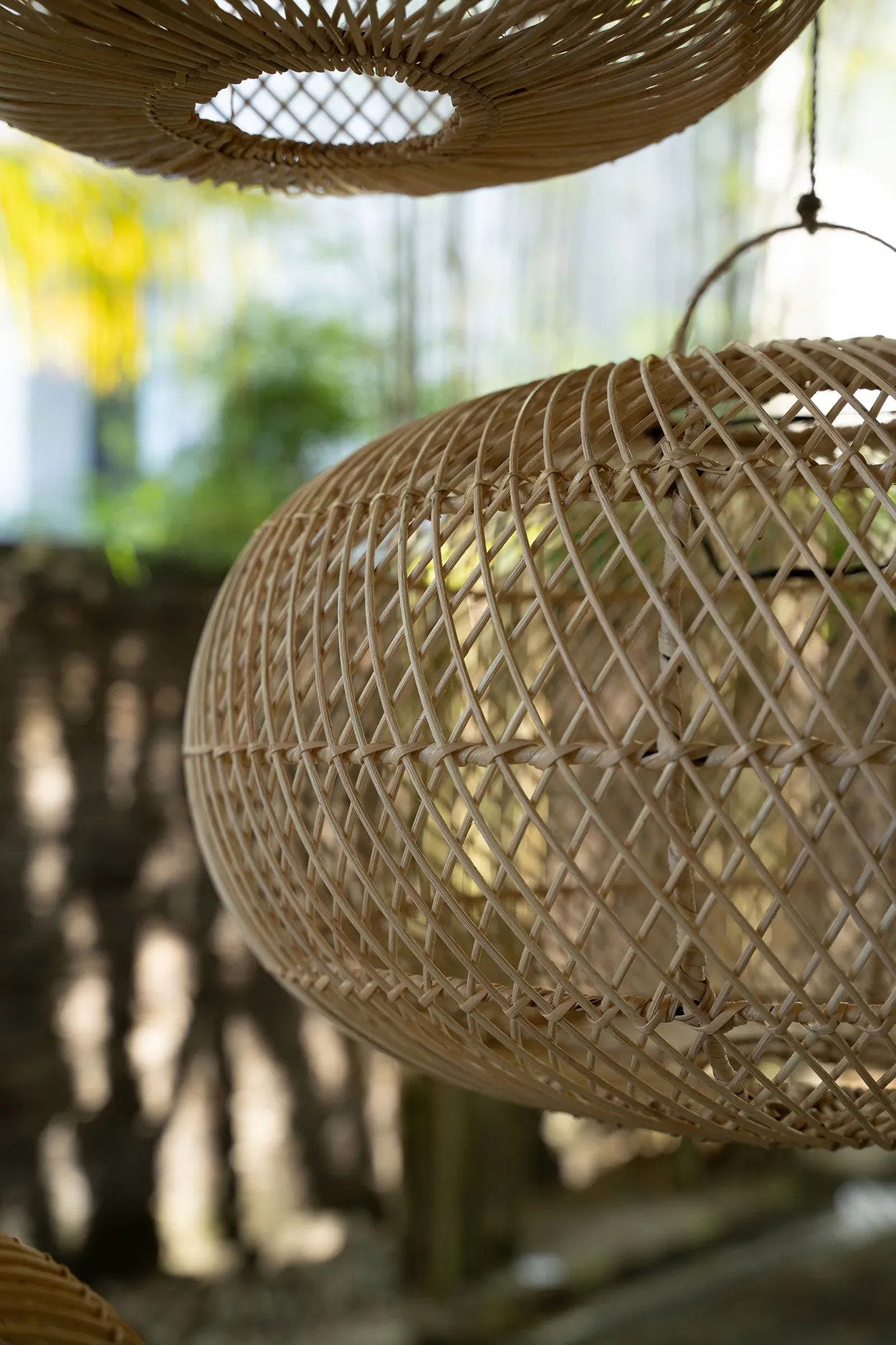 Woven rattan lampshades hanging against a blurred natural background