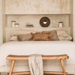 lime wash plaster bedroom with wooden bench, white bedding, and rustic cushions.
