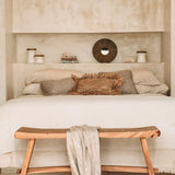 lime wash plaster bedroom with wooden bench, white bedding, and rustic cushions.