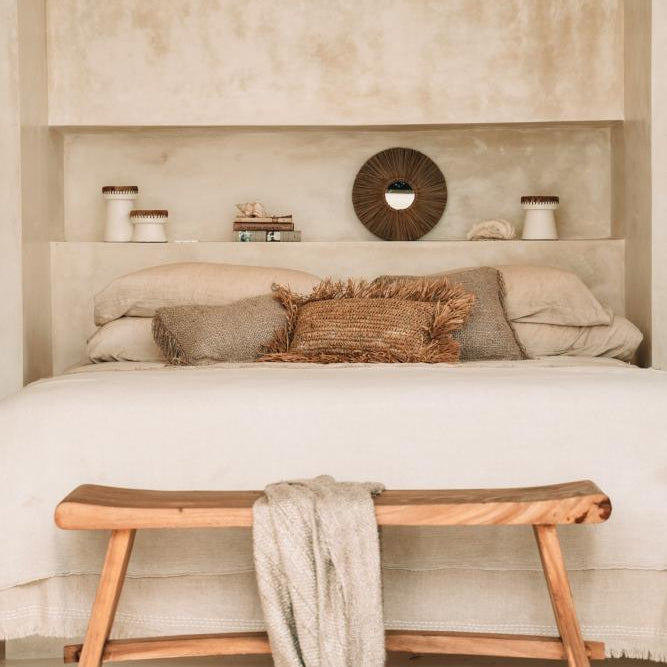 lime wash plaster bedroom with wooden bench, white bedding, and rustic cushions.