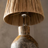 Lamp with a textured base and natural fiber shade against a neutral background