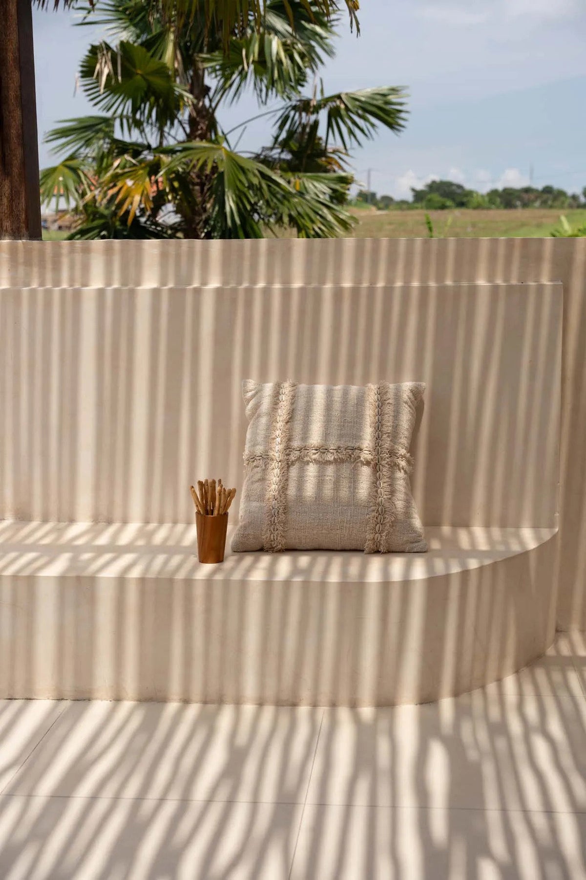 Beige cushion on a curved wall with palm trees and open field in the background