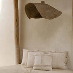 Beige interior with pillows on a bench and a woven lampshade hanging from a thatched roof.
