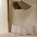 Beige interior with pillows on a bench and a woven lampshade hanging from a thatched roof.