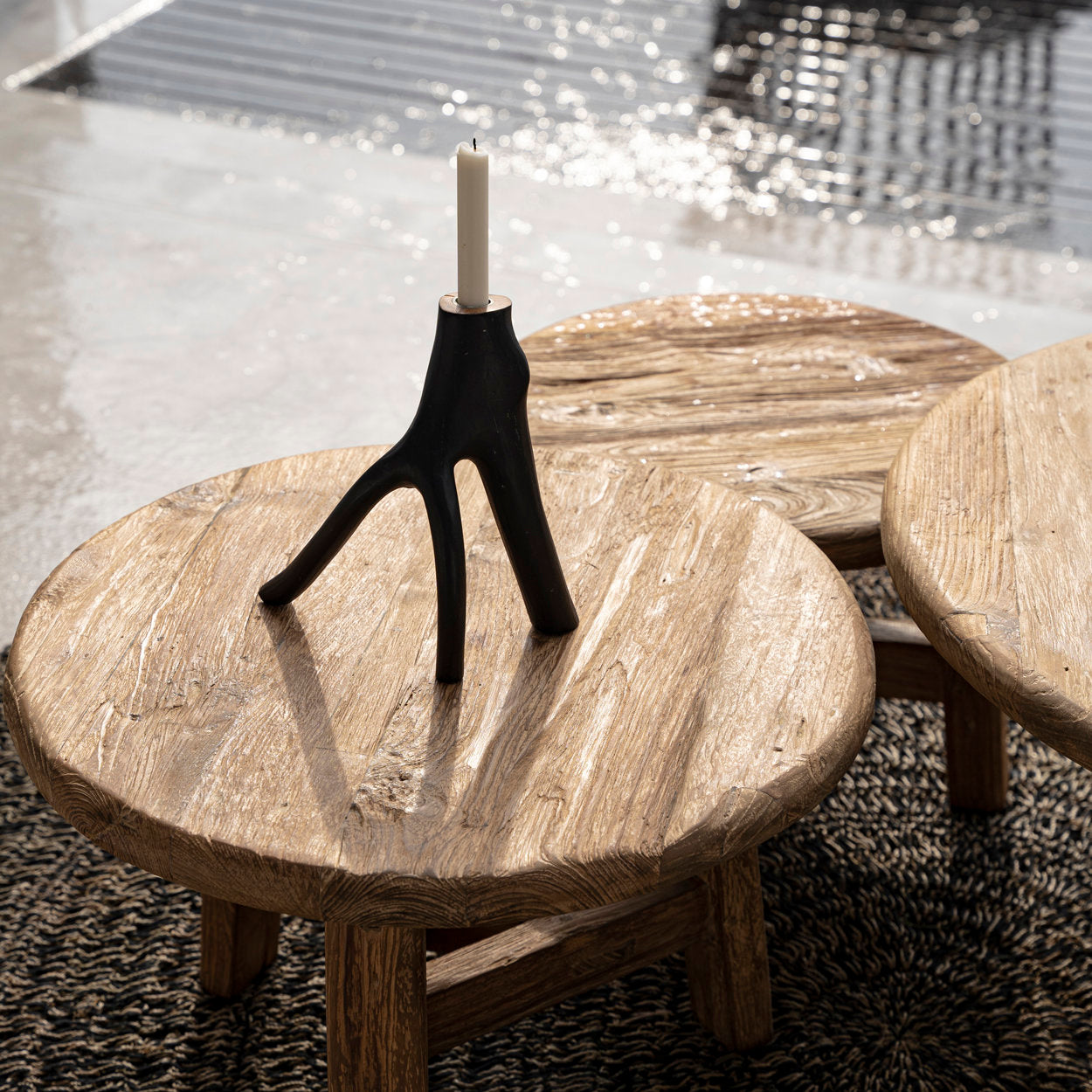 Wooden coffee table with a candle holder and candle on a textured floor.
