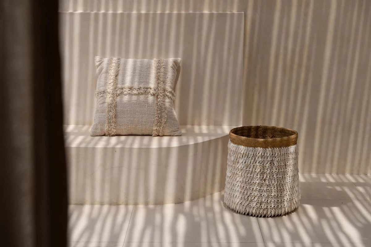 Textured pillow and basket on a striped wall with sunlight casting shadows