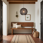 Wooden bench with pillows in a room with a rug, basket, and black wire round pendant light