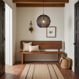 Wooden bench with pillows in a room with a rug, basket, and black wire round pendant light