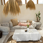 Modern living room with natural sofa, white coffee table, and raffia cushions and rug
.