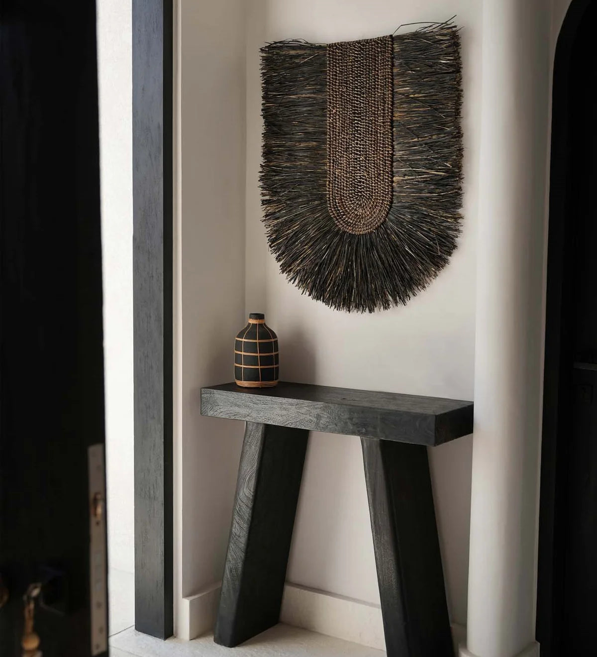 Black Wood Console table with black wall hanging in a limewash plastered room