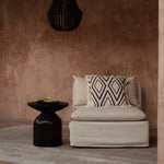 Beige sofa with patterned pillow against a brown wall with a black pendant light.