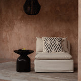 Beige sofa with patterned pillow against a brown wall with a black pendant light.