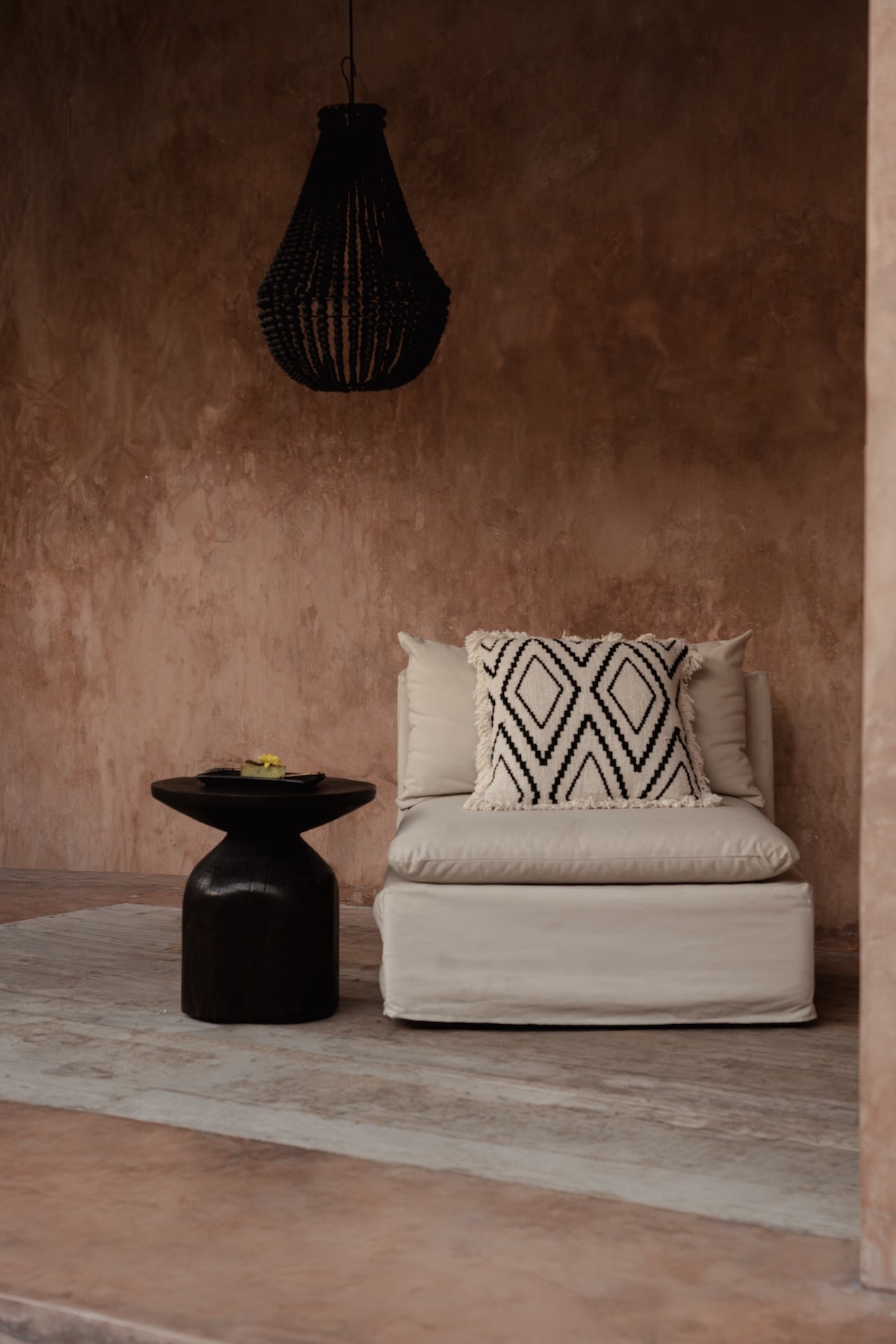 Beige sofa with patterned pillow against a brown wall with a black pendant light.