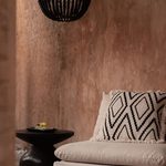Beige sofa with patterned pillow and black chandelier side table against a textured wall.