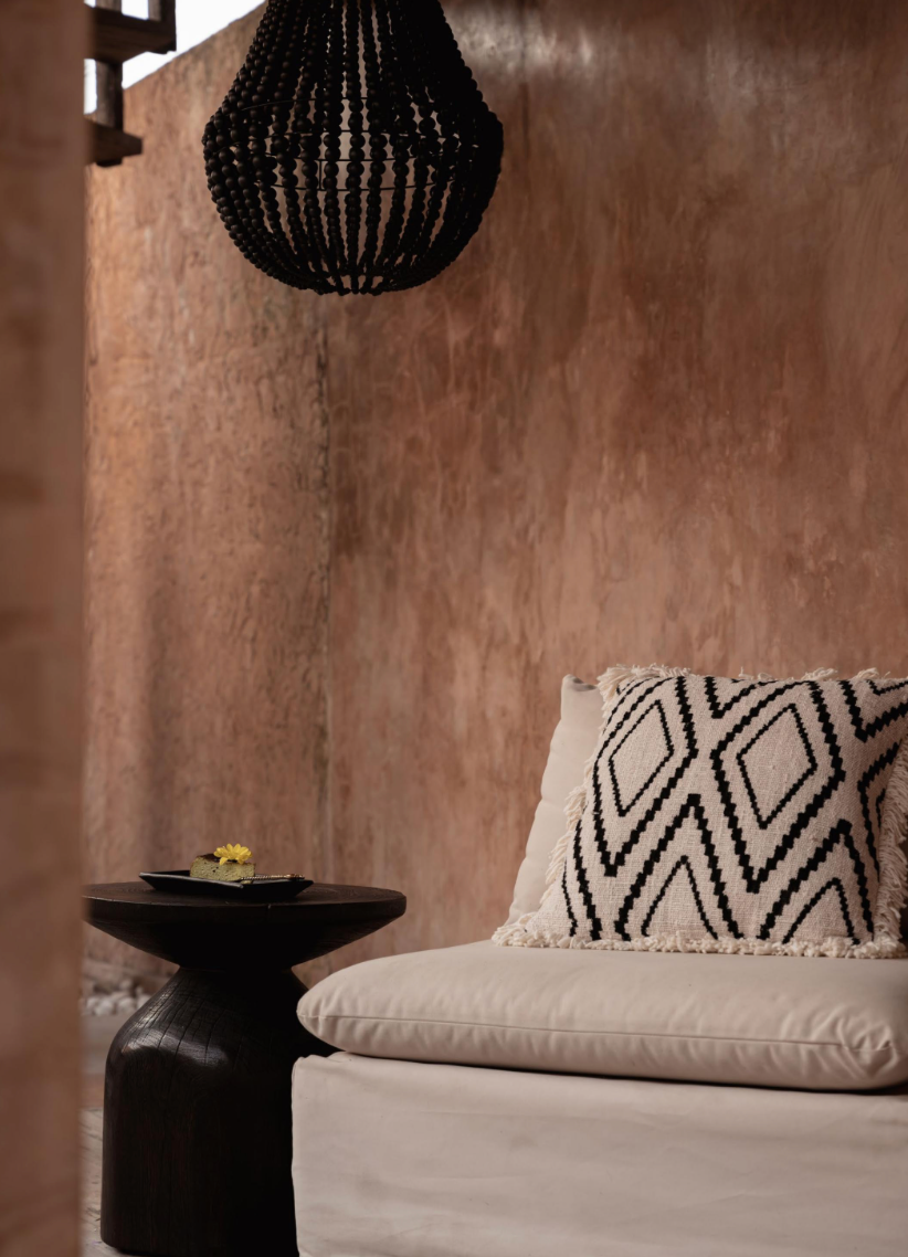 Beige sofa with patterned pillow and black chandelier side table against a textured wall.