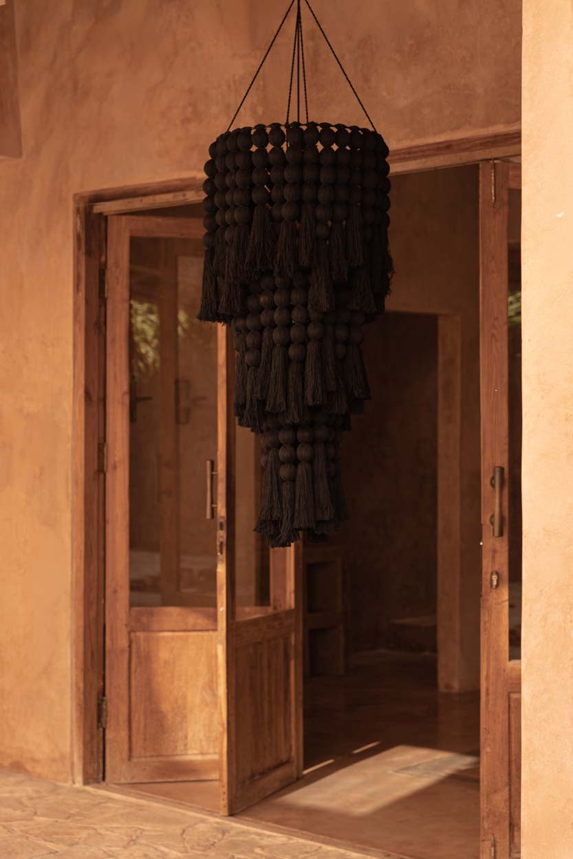 Black woven chandelier hanging in a room with wooden doors and beige walls.